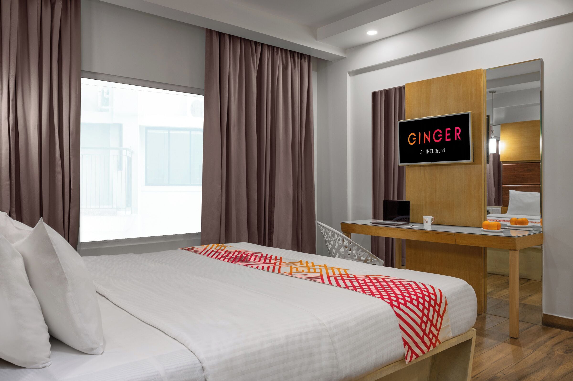 A hotel room with a bed, a desk, a laptop, and a sign that reads "GINGER An IHC Hotels Brand".