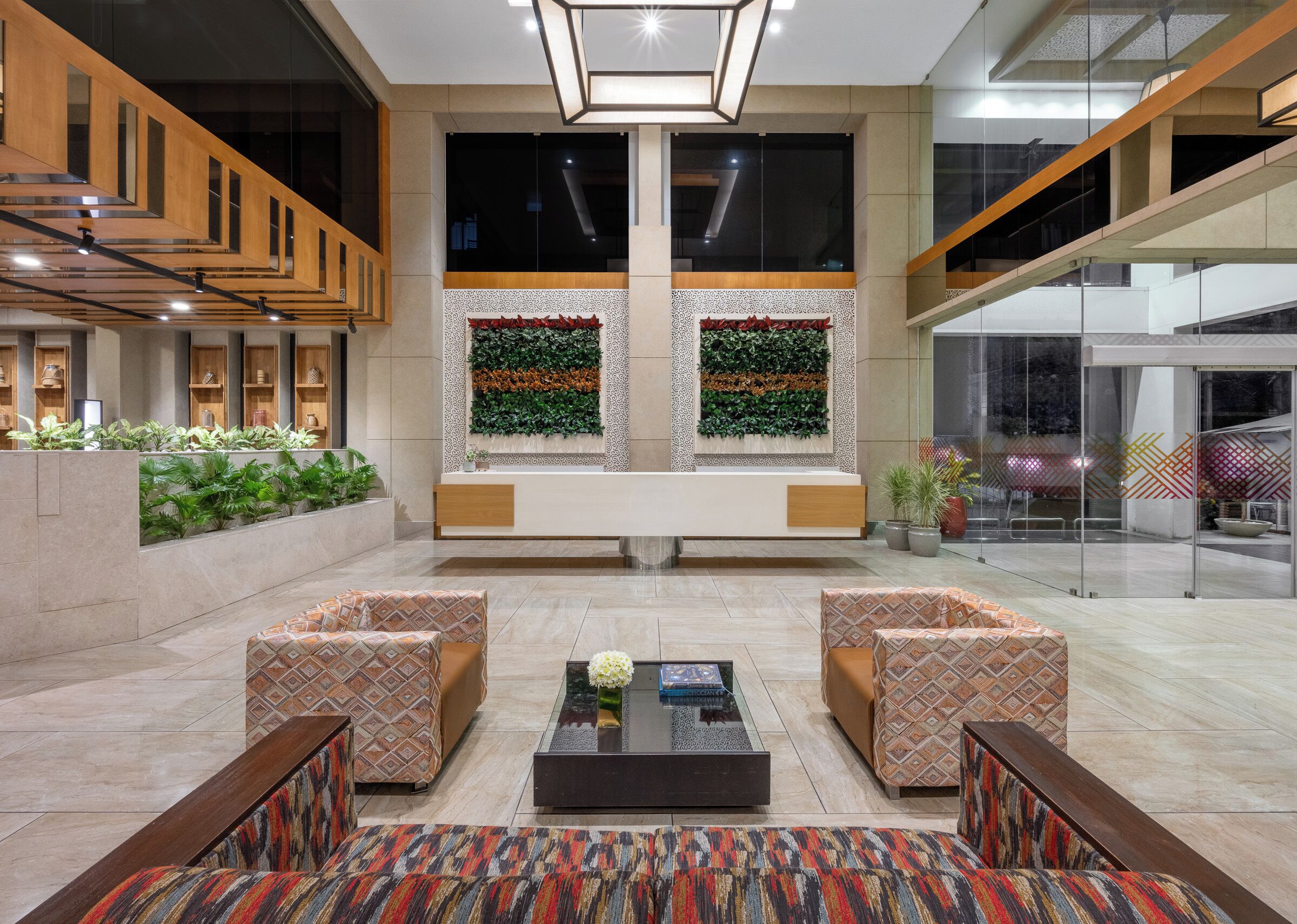 A modern lobby with a reception desk, two patterned sofas, a coffee table, and a large window with a green wall.