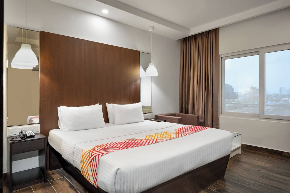 A hotel room with a large bed, a bedside table with a phone, a mirror, and a window with curtains.