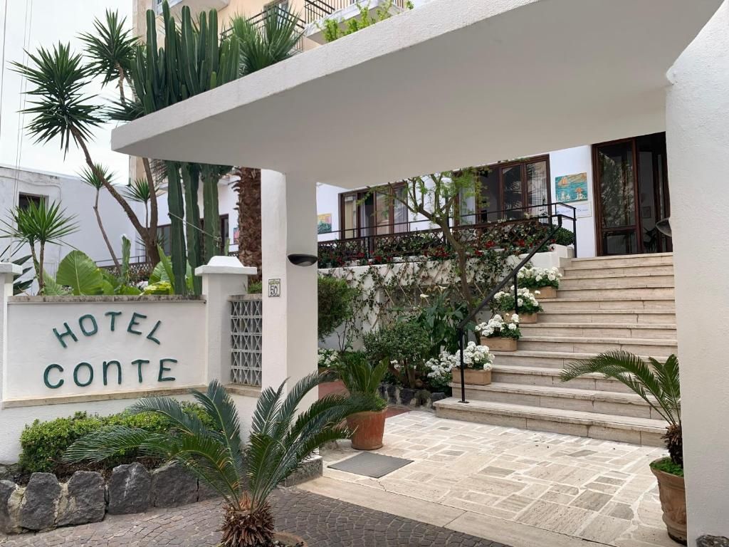 A hotel entrance with a sign reading 'HOTEL CONTE,' a covered staircase, and a variety of plants.