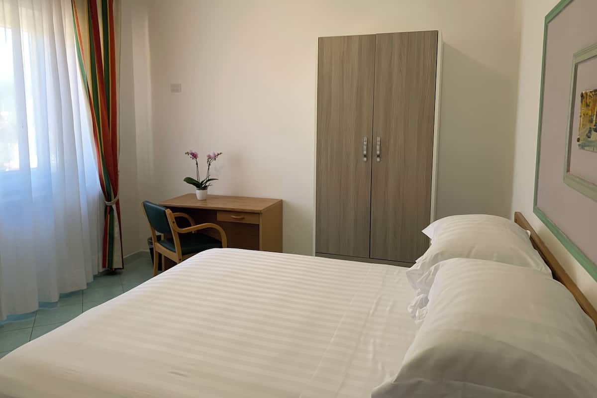 Ein Hotelzimmer mit Bett, Schreibtisch, Stuhl, Kleiderschrank und einem Fenster mit Vorhängen.