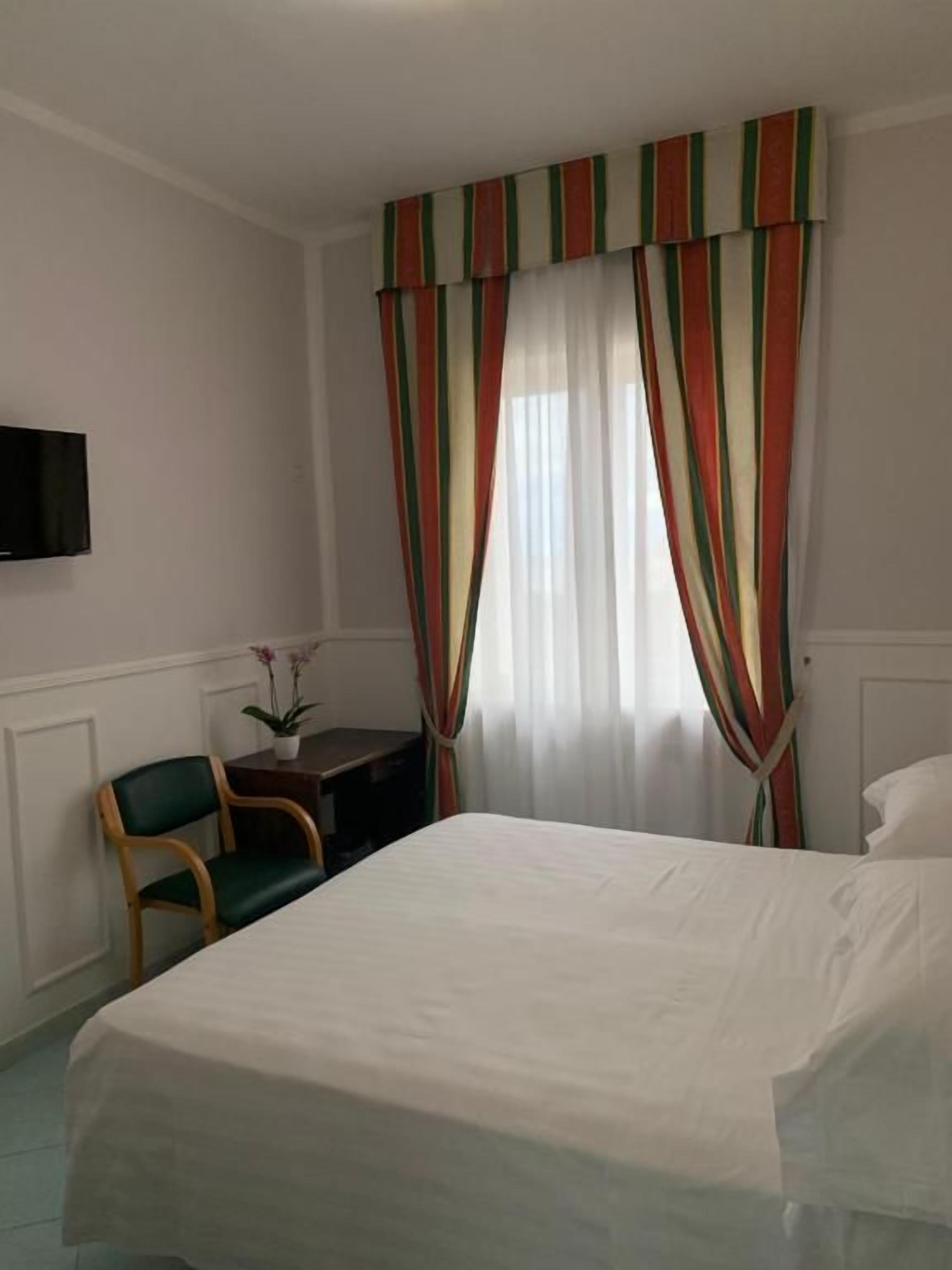 Hotellihuone, jossa on sänky, tuoli, työpöytä ja seinälle asennettu televisio.
