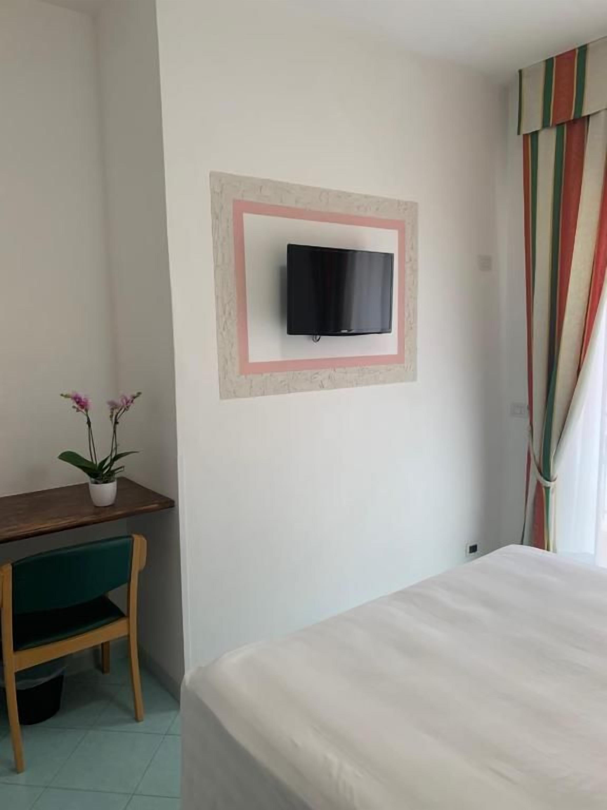 A room with a bed, a desk with a chair, a potted plant, and a mounted television.