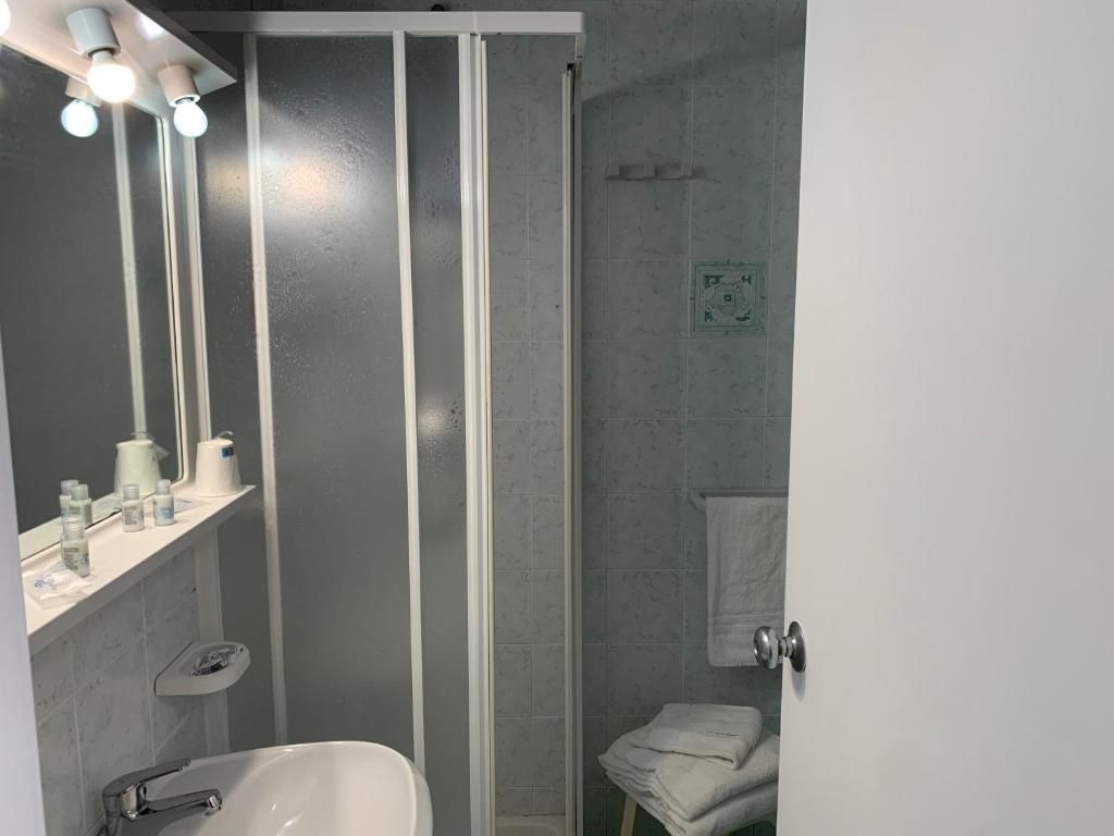 Ein Badezimmer mit Dusche, Waschbecken und Toilette. Über dem Spiegel befinden sich Lampen und eslen sich ein Handtuchhalter.