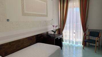 Una habitación de hotel con cama, escritorio, computadora, silla y ventana con cortinas.