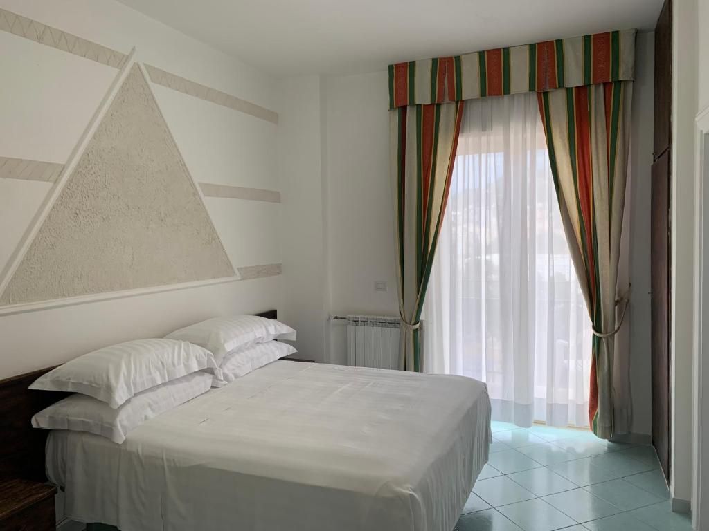Habitación de hotel con cama, radiador, ventana con cortinas y un diseño geométrico en la pared.