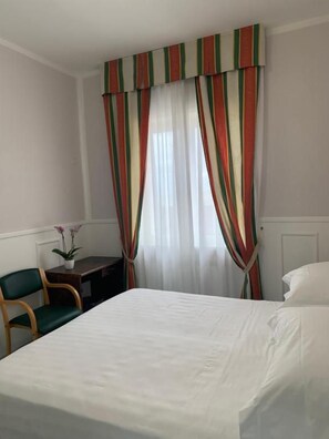 A hotel room with a bed, a desk, a chair, and curtains.