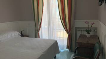 Una camera d'albergo con un letto, una sedia, un tavolino e tende, con una pianta in vaso.