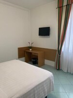 Habitación de hotel con cama, escritorio, televisión y ventana con cortinas.