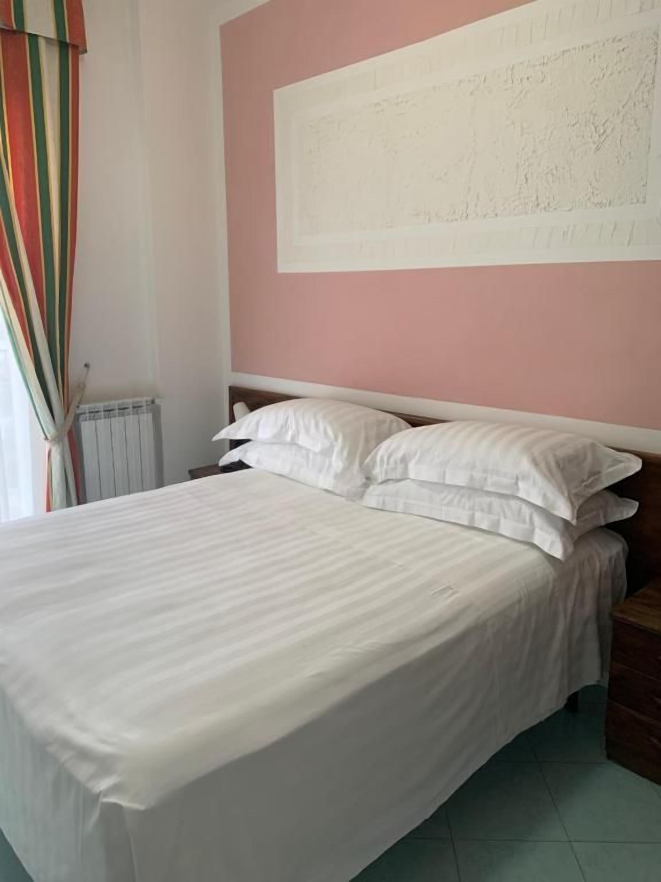 Ein Bett mit weißer Bettwäsche in einem Zimmer mit einer rosafarbenen Wand und einem großen, weißen Kunstwerk darüber.