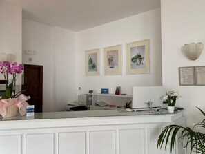 A reception desk with framed artwork on the wall, a computer, and a plant.