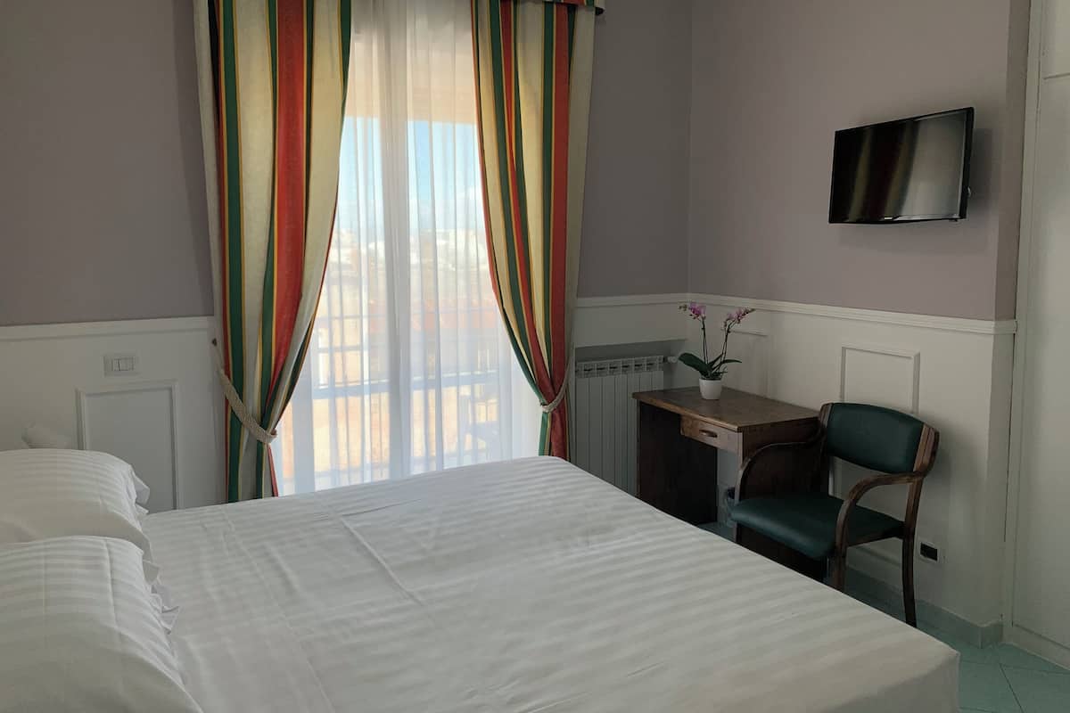 Ein Hotelzimmer mit Bett, Schreibtisch mit Stuhl, Wandfernseher und einem Fenster mit Vorhängen.
