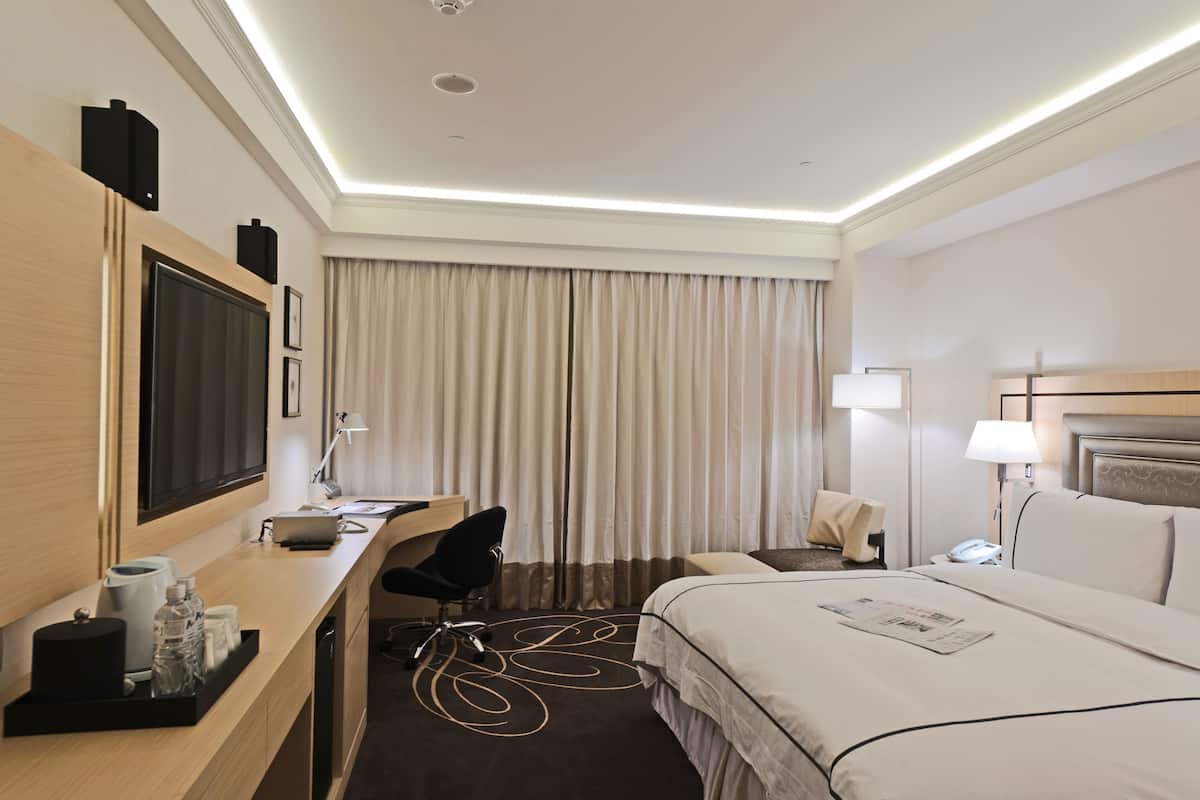 Ein Hotelzimmer mit Bett, Schreibtisch, Stuhl, Fernseher und Vorhängen.