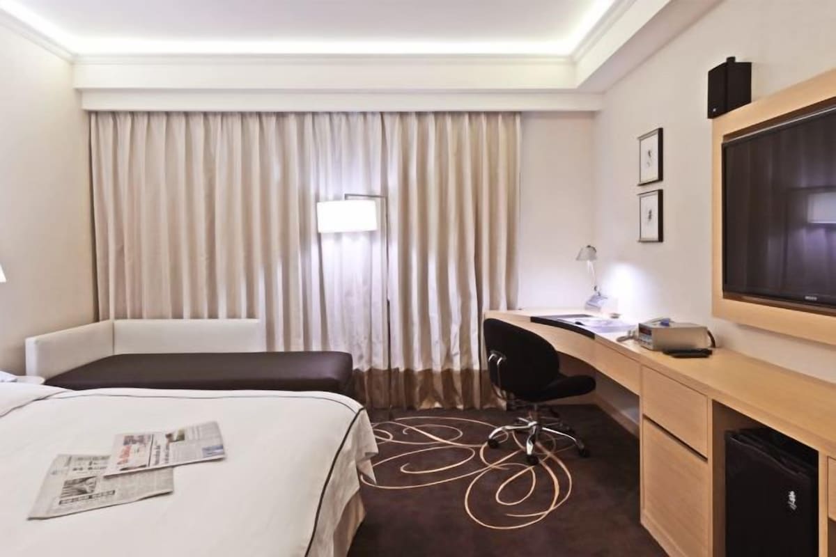 A hotel room with a bed, a desk, a chair, a television, and a window with curtains.