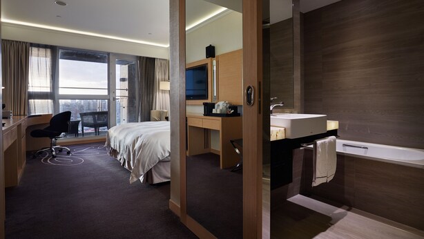 Une chambre d’hôtel moderne équipée d’un lit, d’un bureau, d’une chaise et d’une grande fenêtre donnant sur la ville.