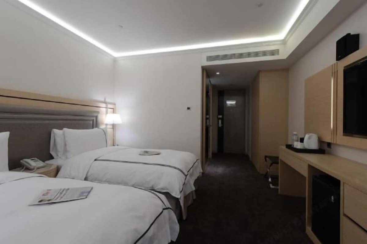A hotel room with two beds, a desk, a TV, and a bathroom visible through an open door.