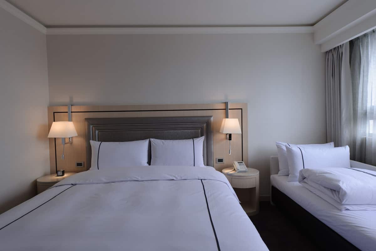 Ein Hotelzimmer mit einem großen Bett, zwei Nachttischen inklusive Lampen, einem Telefon am Nachttisch und einem Fenster mit Vorhängen.