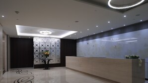 Un espace d’accueil moderne, doté d’un comptoir de réception en marbre, d’un motif géométrique sur les murs et d’un lustre.