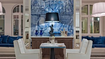 Ein Essbereich mit Schachbrettmuster-Boden, einem Tisch mit Stühlen, einer blauen Wand mit Kacheln und Kunstwerken sowie blauen, gepolsterten Sofas.