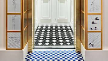 An elevator with a checkered floor, framed artwork on the walls, and a double door.