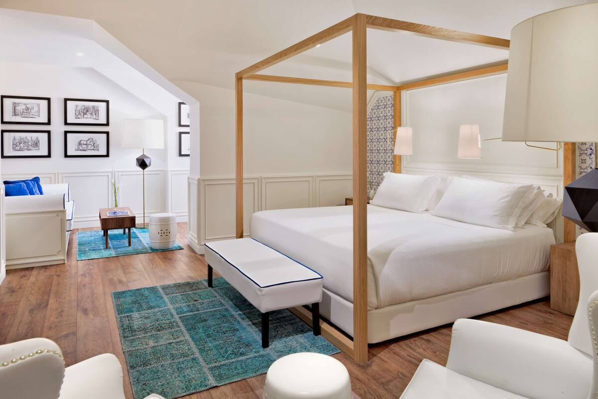 Een moderne slaapkamer met een hemelbed, een zithoek met een bankje, en een tafeltje met een vaas.