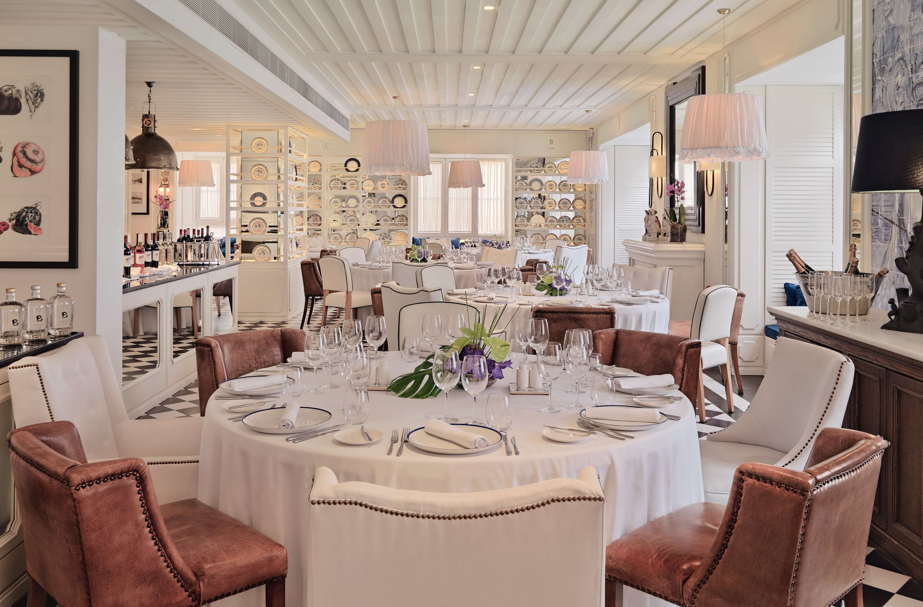 A dining area with round tables set for multiple guests, featuring white tablecloths and brown leather chairs.