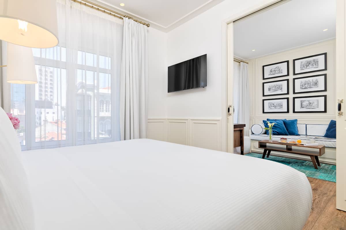 Een hotelkamer met een groot bed, een aan de muur bevestigde televisie, en een zithoek met een tafel en stoelen.