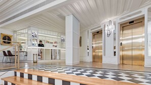 Un vestíbulo moderno con piso a cuadros, una escalera, un mostrador de recepción y dos ascensores.