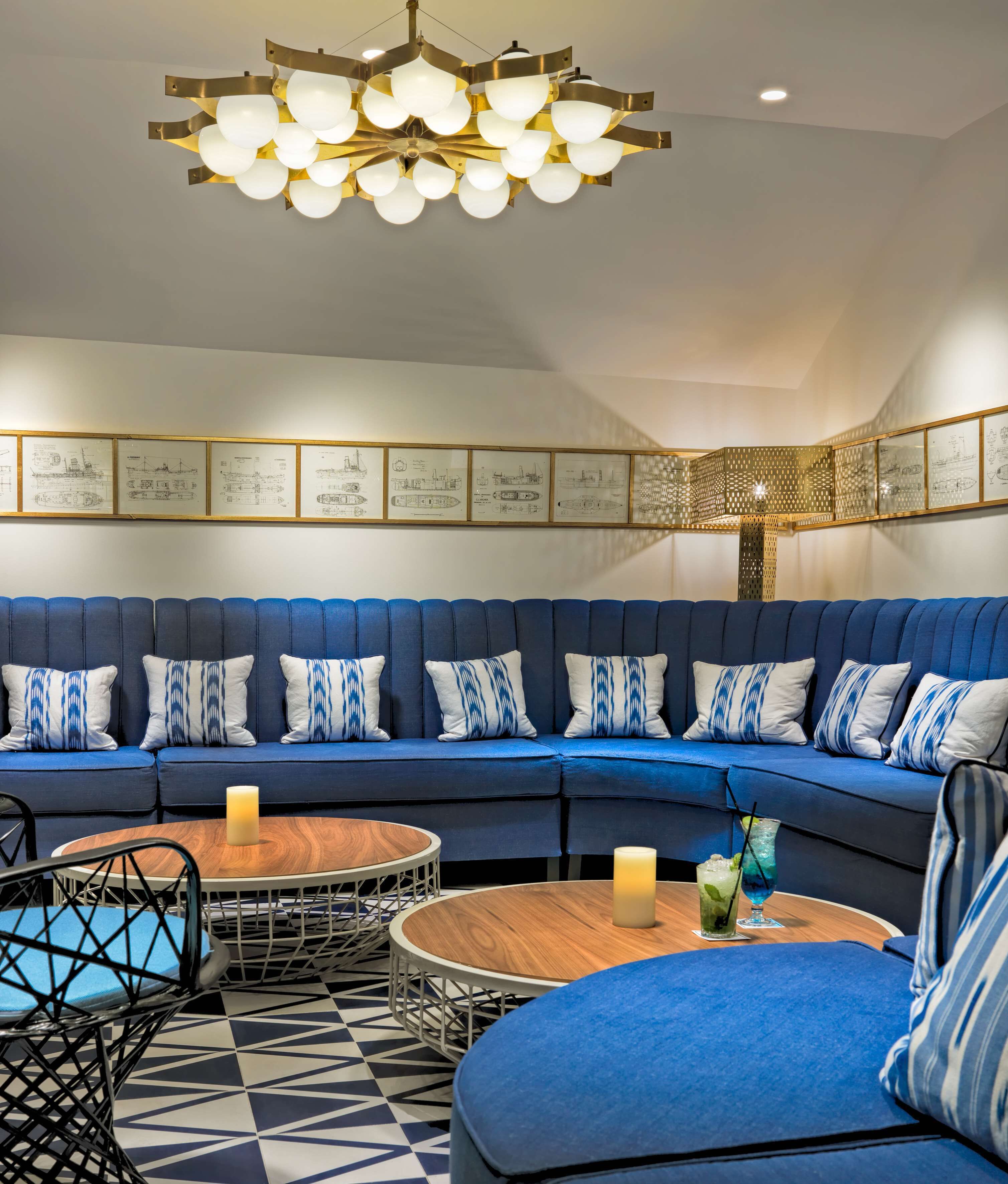 A modern lounge area with a blue sofa set, round wooden tables, and a unique chandelier.