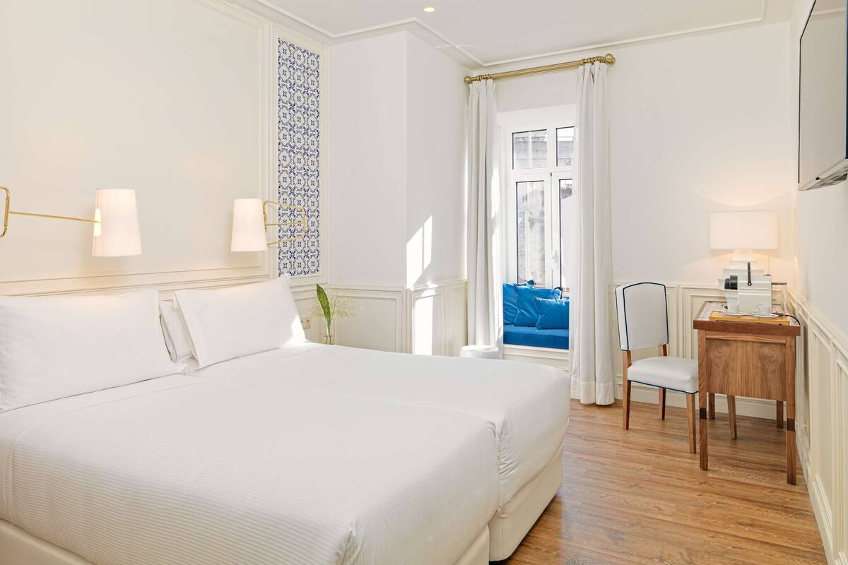 Hotelkamer met een groot bed, een bureau met stoel, een raam met gordijnen en uitzicht op buiten.