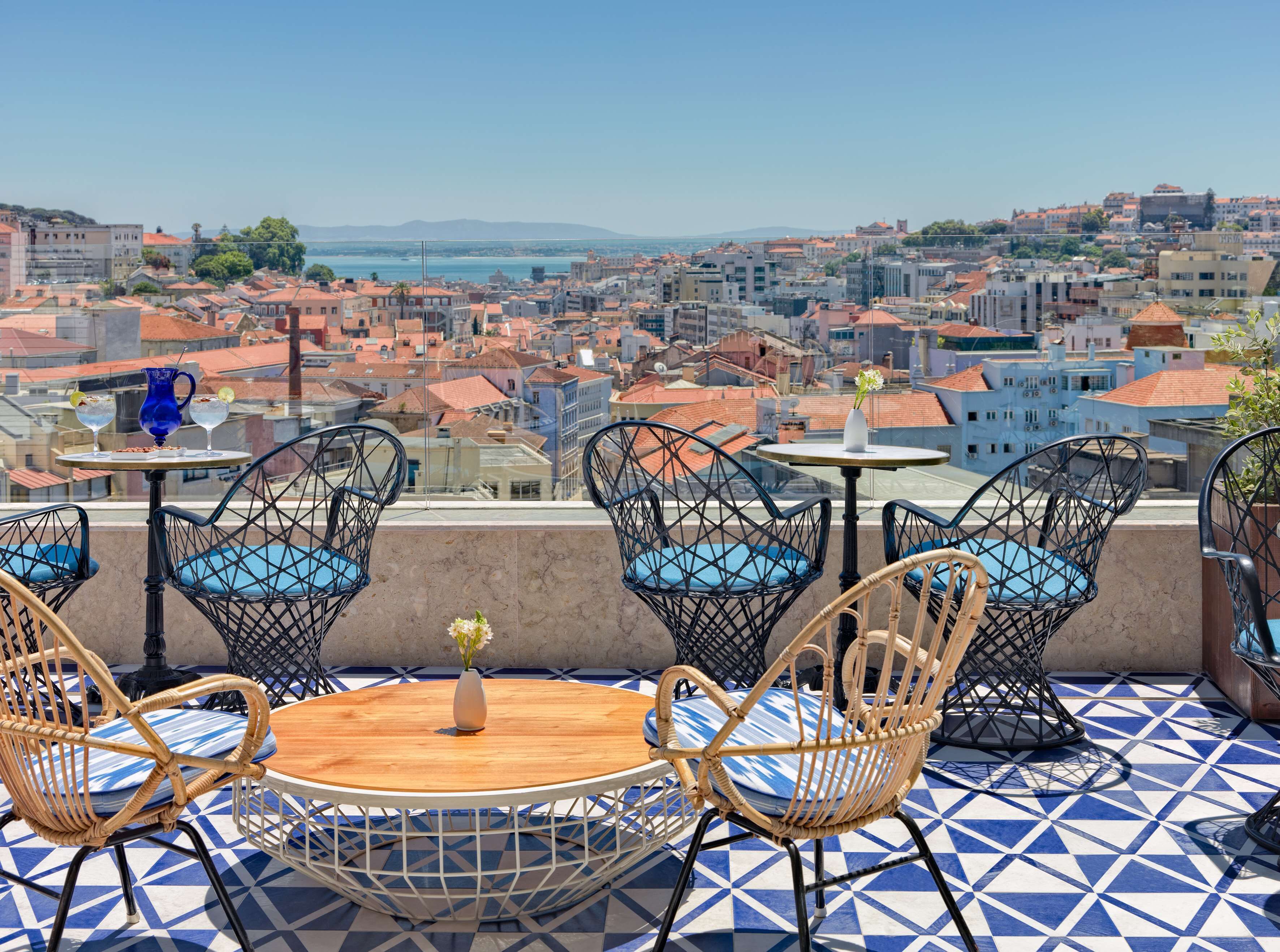 A terrace with wicker chairs, a round table, and a view of a cityscape.