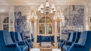 Una sala de estar lujosa con un gran ventanal, sillones azules, una mesa de centro blanca y una araña.