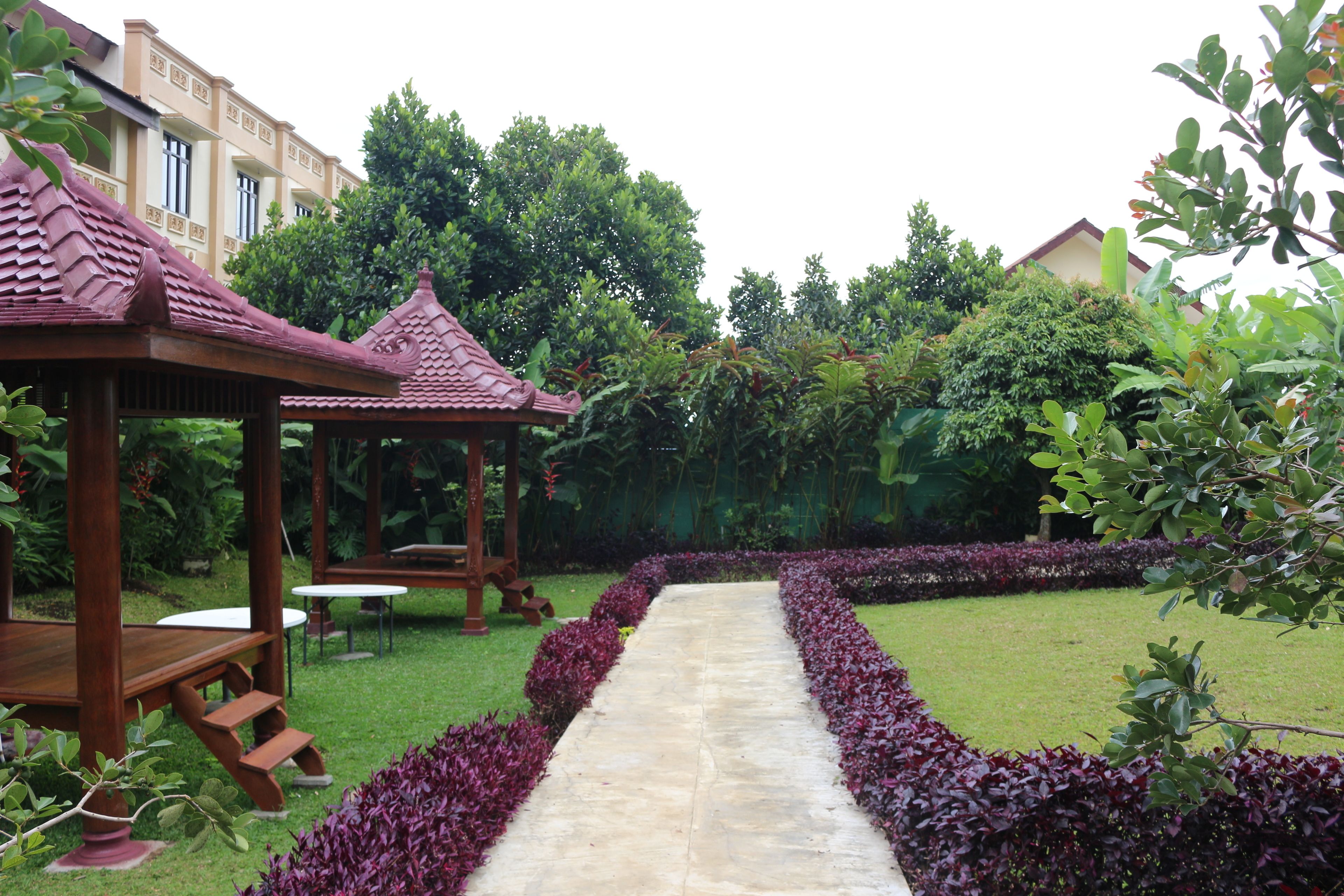A garden with a stone pathway, wooden gazebo, and neatly trimmed hedges.