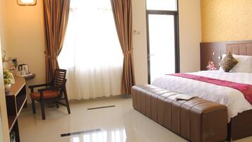 A hotel room with a bed, a seating area, a desk with a kettle, and a window with curtains.