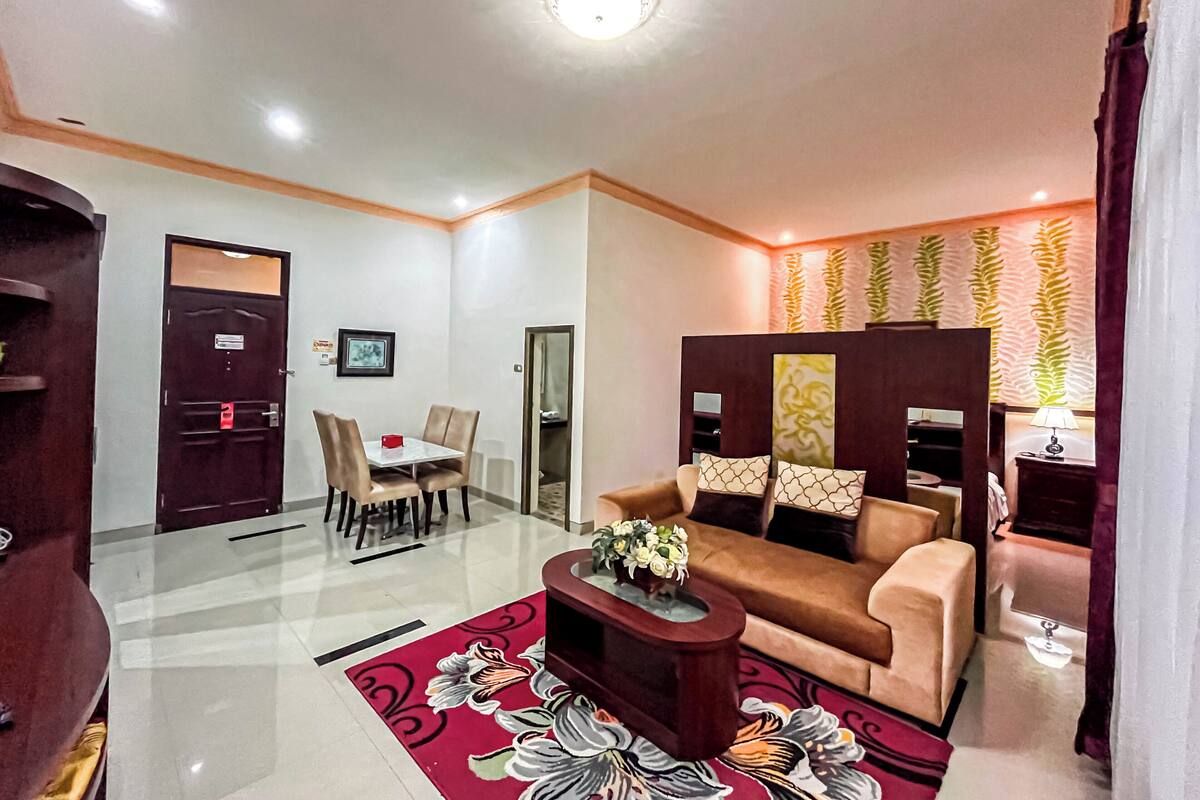 A modern living room with a sofa, a coffee table with flowers, a dining area with a table and chairs, and a decorative wall with leaf patterns.