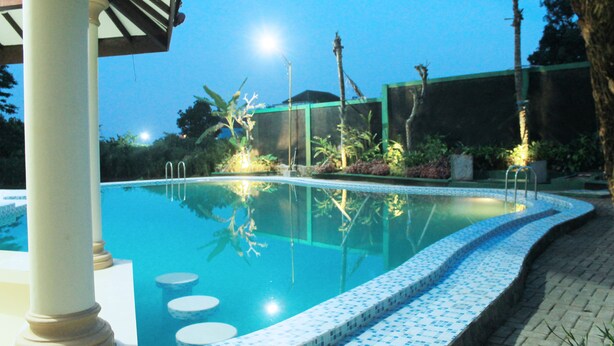 A swimming pool with a tiled edge, surrounded by plants and a pergola structure. - Zamzam Hotel and Convention Batu Powered by Archipelago (Batu)