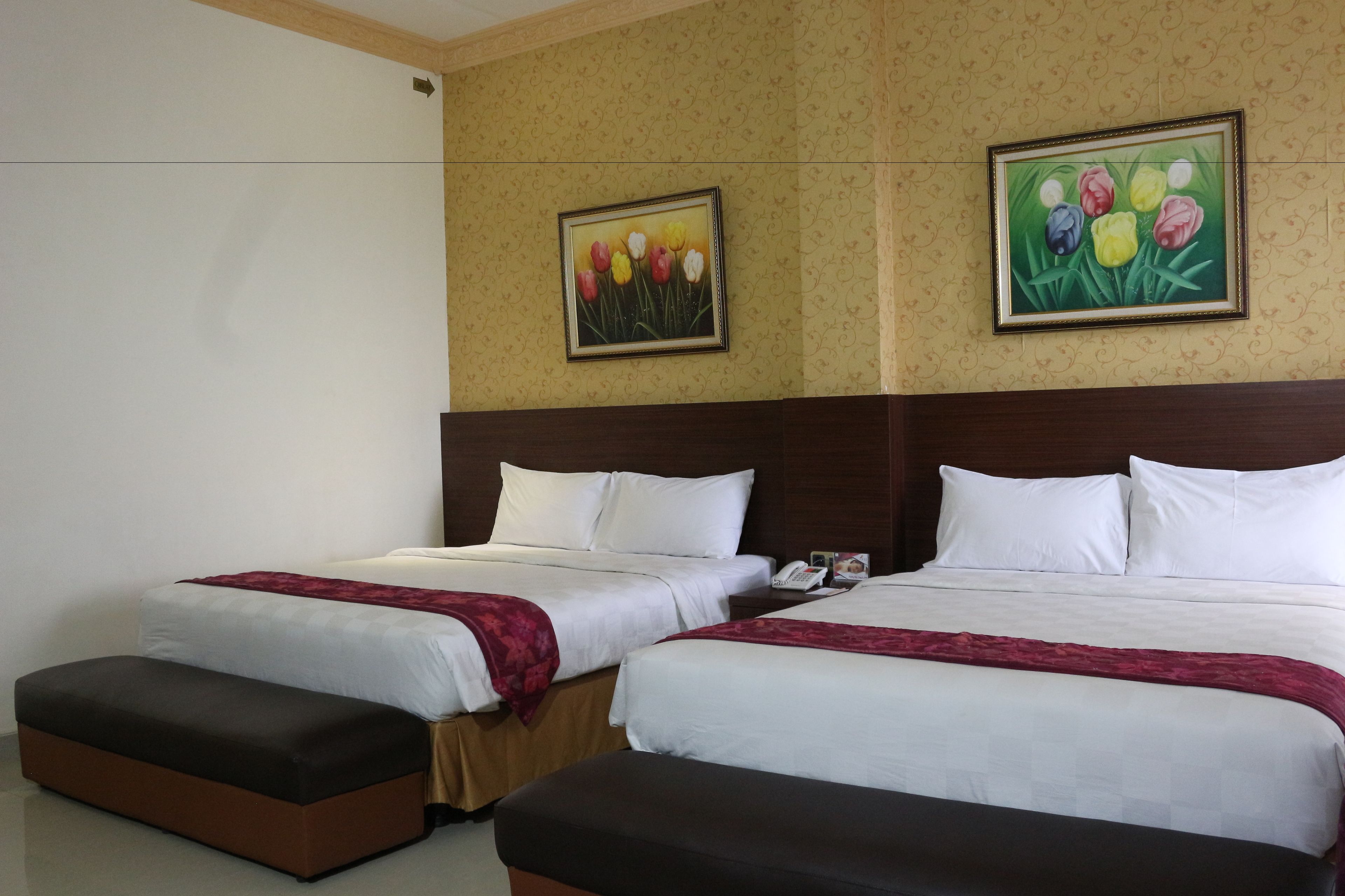 Habitación de hotel con dos camas, cada una con ropa blanca y una manta roja. Hay dos cuadros de tulipanes en la pared.