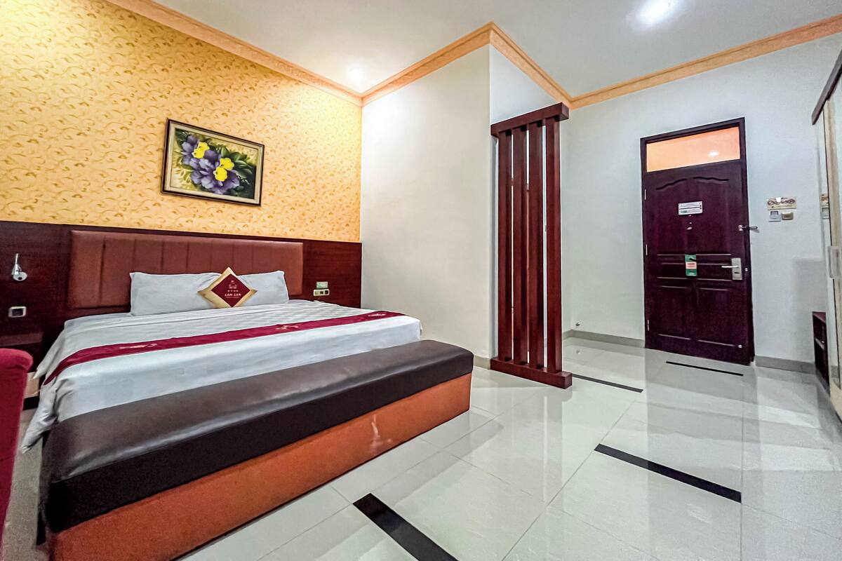 A hotel room with a bed, a wooden headboard, a painting on the wall, and a wardrobe.