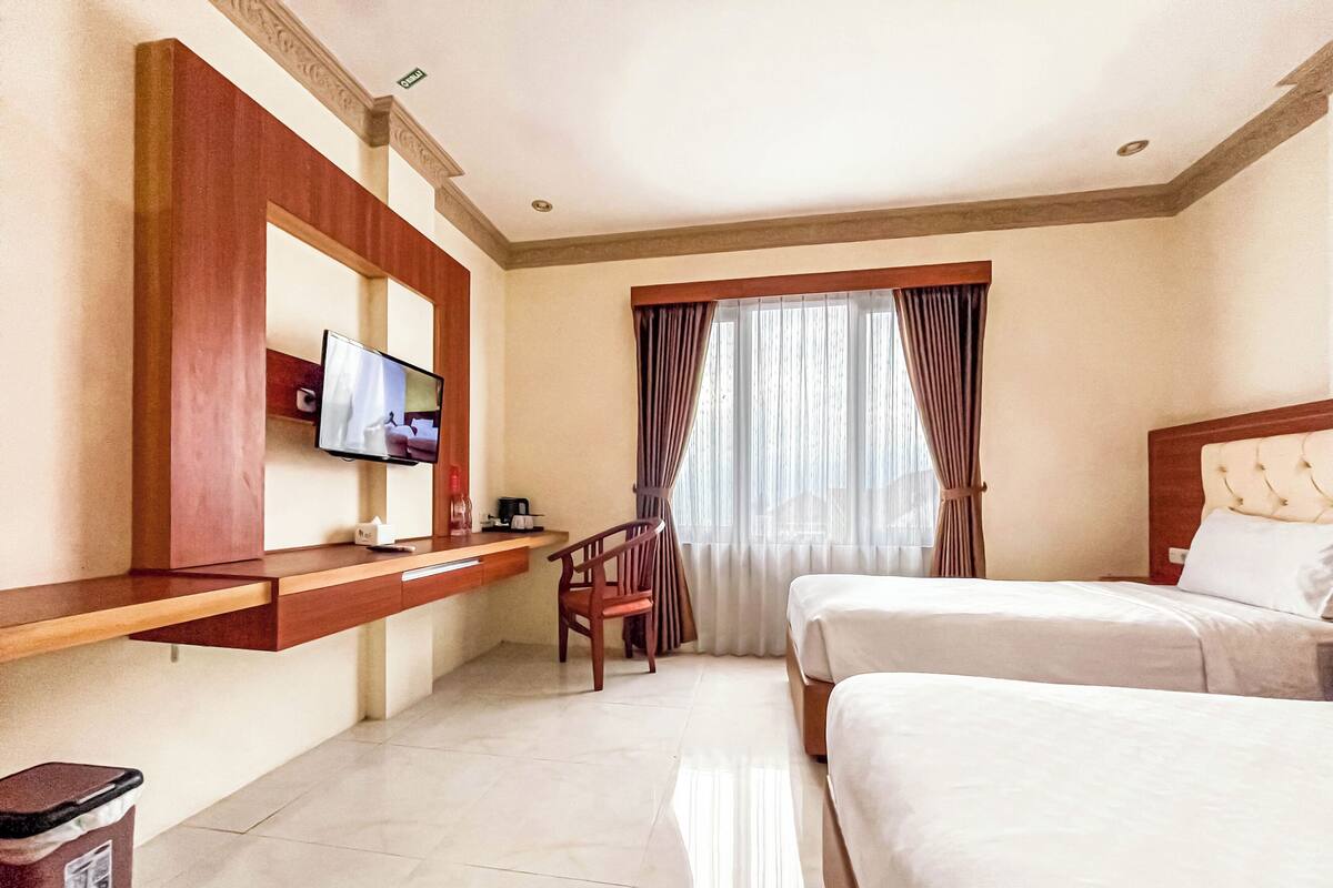 A hotel room with a bed, a desk with a TV, a chair, and a window with curtains.
