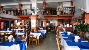 A restaurant with multiple dining tables covered with blue tablecloths, wooden chairs, and fans. - Dee-Lek Guesthouse and Restaurant (Cha-am)