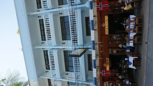 A multi-story building with balconies, a restaurant area with tables and chairs, and a visible flag. - Dee-Lek Guesthouse and Restaurant (Cha-am)