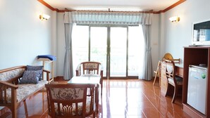 A room with a sofa, dining table, chairs, a TV, and a refrigerator. - Dee-Lek Guesthouse and Restaurant (Cha-am)