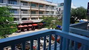 A multi-story building with balconies, a restaurant with red umbrellas, and parked cars. - Dee-Lek Guesthouse and Restaurant (Cha-am)