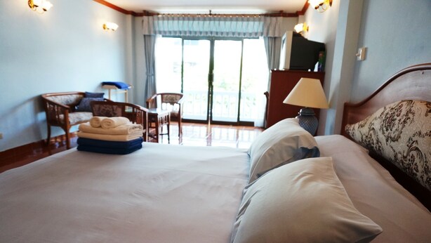 A hotel room with a large bed, a desk with a chair, a small table with a lamp, and a balcony with a view. - Dee-Lek Guesthouse and Restaurant (Cha-am)