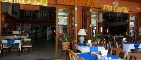 A restaurant with a wooden interior, tables set with blue tablecloths, and a sign reading "DEE-LEEK".