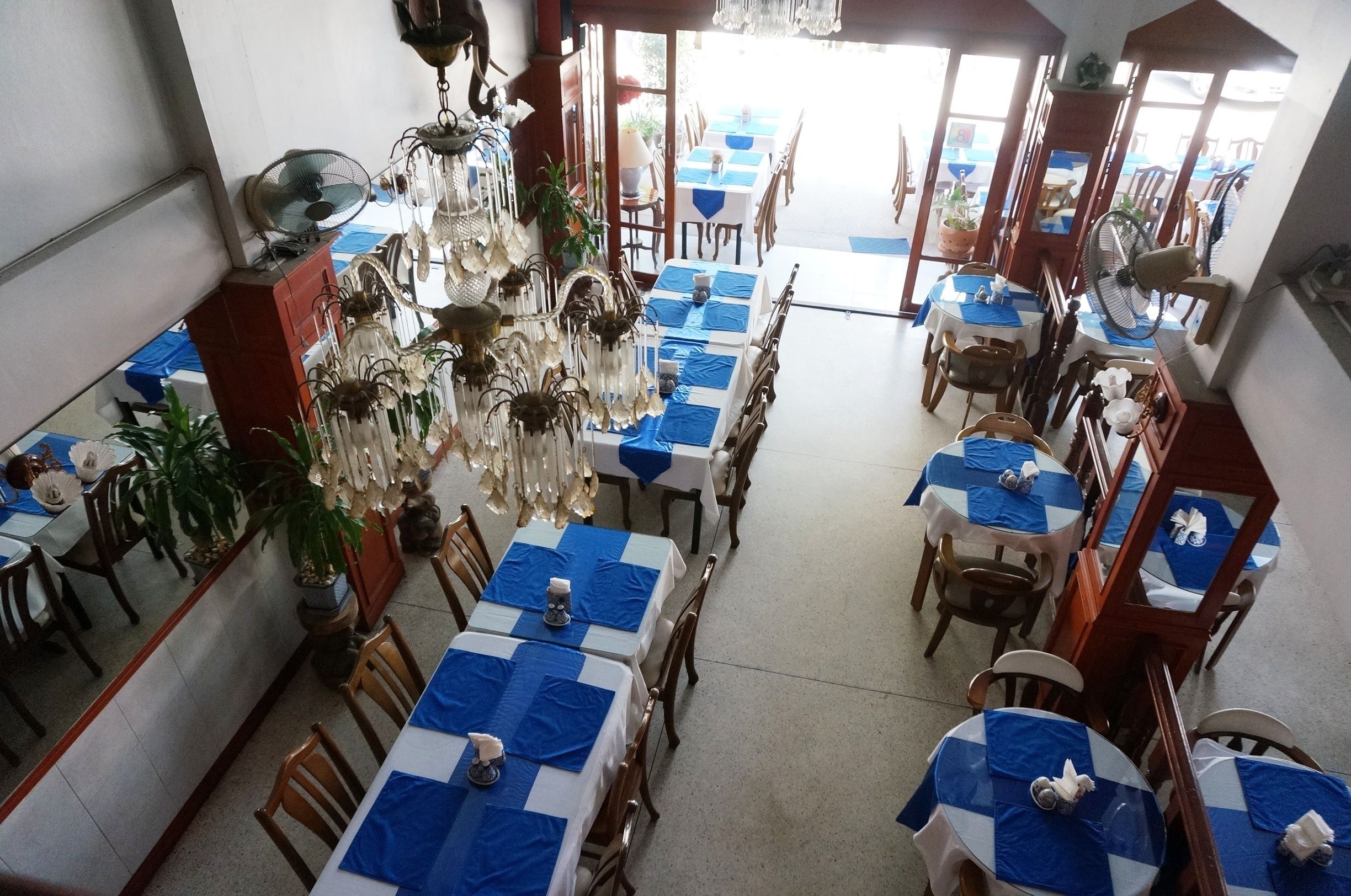A restaurant with tables covered in blue tablecloths, wooden chairs, and hanging chandeliers.