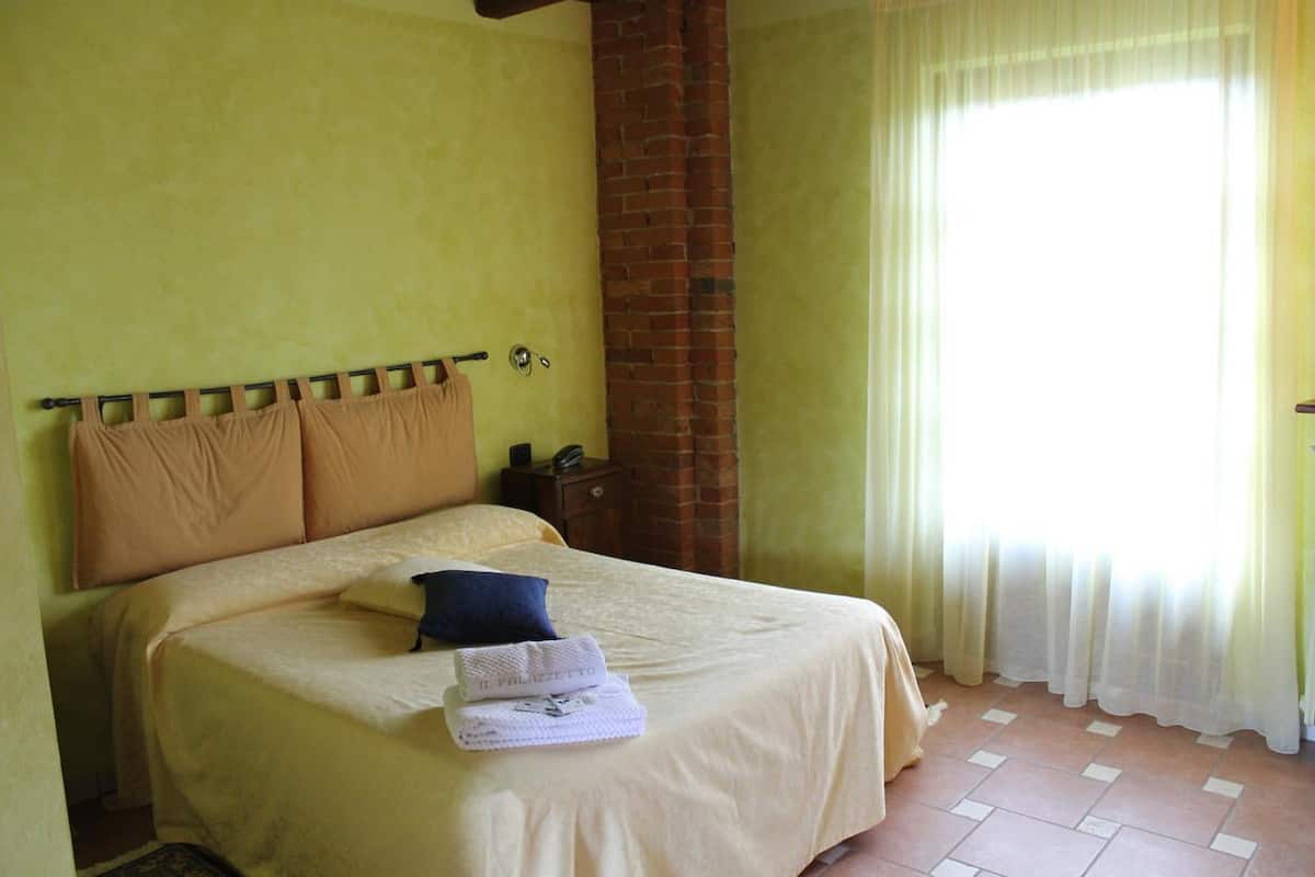 A hotel room with a bed, a nightstand, a brick wall, and a window with curtains.