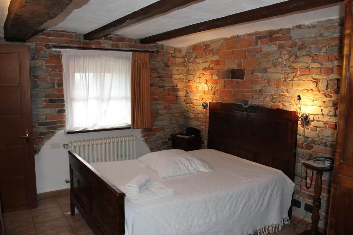 A bedroom with a stone wall, a wooden bed, a nightstand, and a window with curtains.
