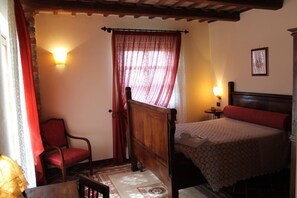 Um quarto aconchegante com uma cama de madeira, uma cadeira vermelha, uma mesinha e uma janela com cortinas vermelhas.