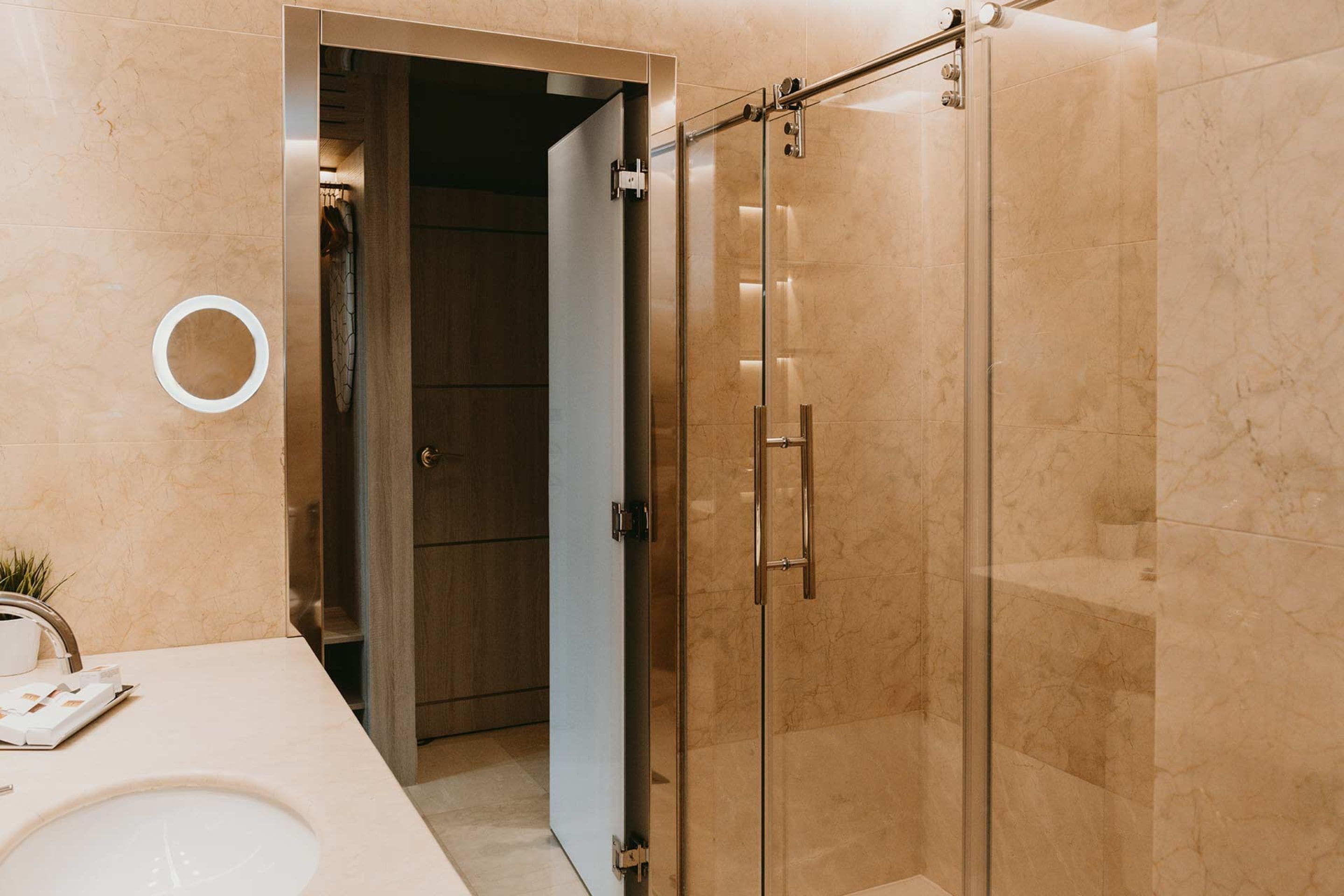 A modern bathroom with a glass shower enclosure, a round mirror, and a white sink.
